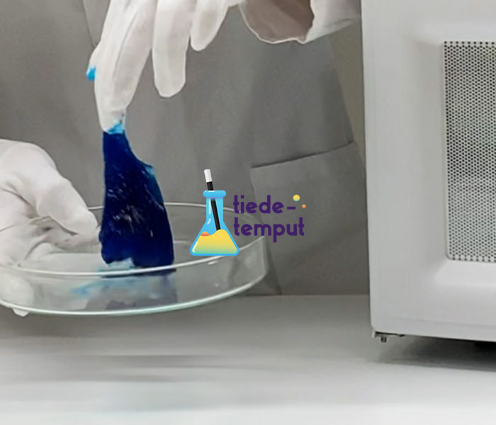 Tutkija nostaa sinisen limaklöntin petrimaljasta. Keskellä Tiedetemppu logo.