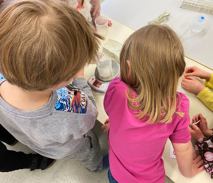 Lapset mittaavat nestettä dekantterilasiin, joka on vaa'alla.
